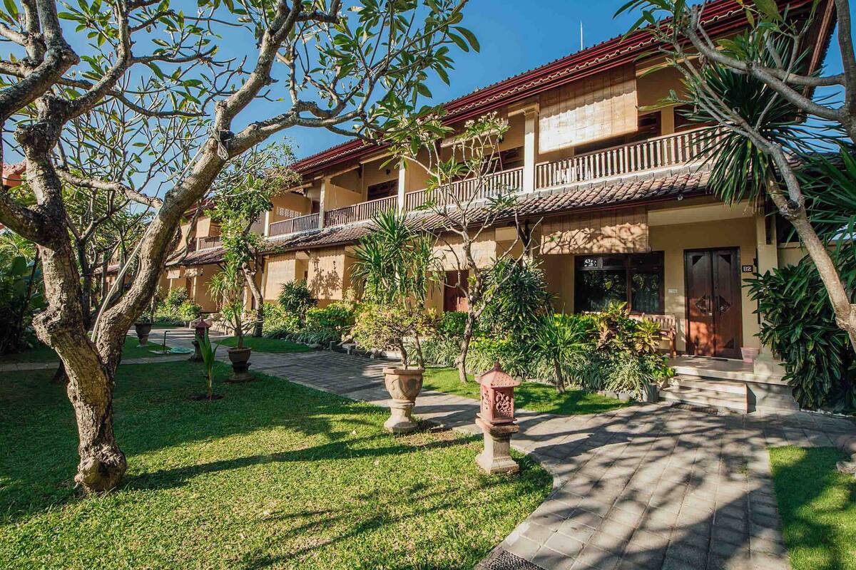 A two-story building with a balcony, surrounded by a well-maintained garden with potted plants and a stone pathway.