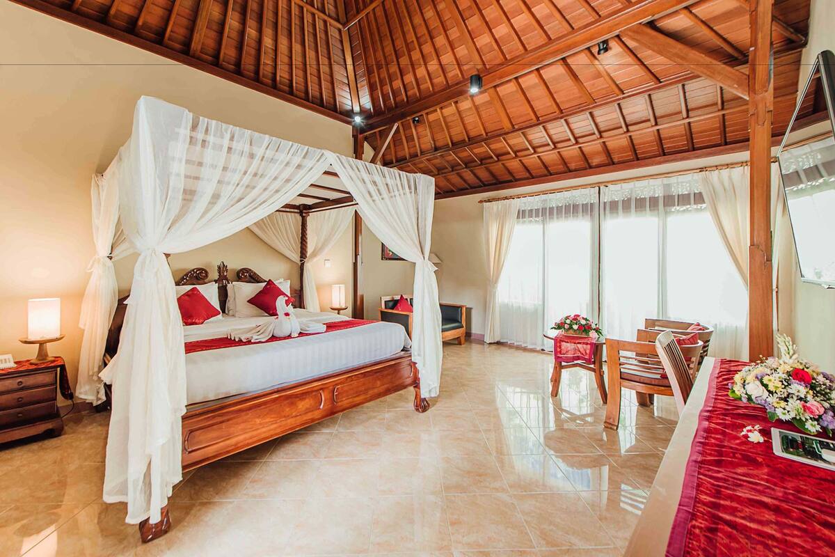 A spacious bedroom with a large bed, a wooden ceiling, and a dining area with a table set for two.