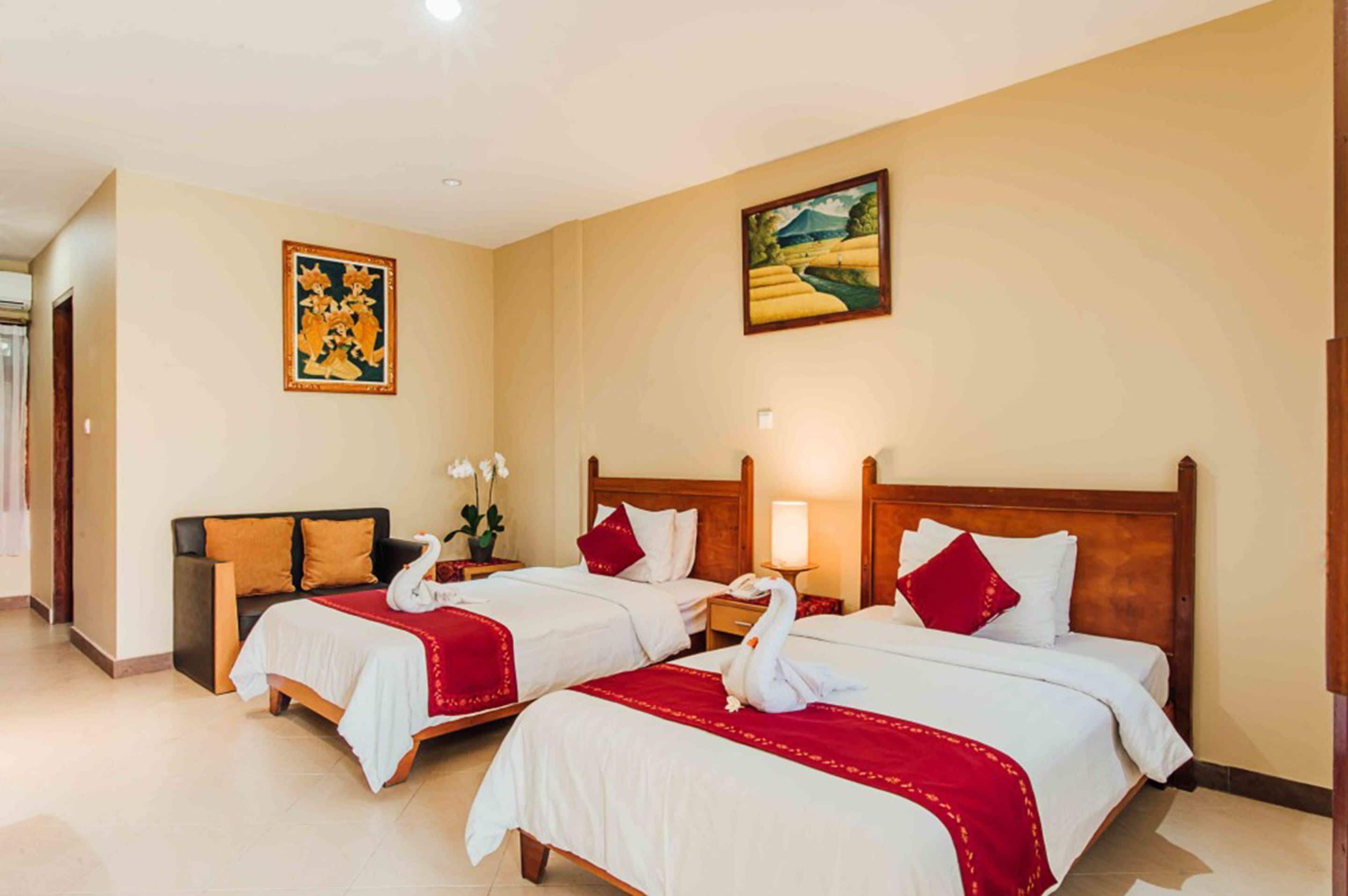 A hotel room with two beds, each with white linens and red accents, a wooden headboard, and a painting on the wall.