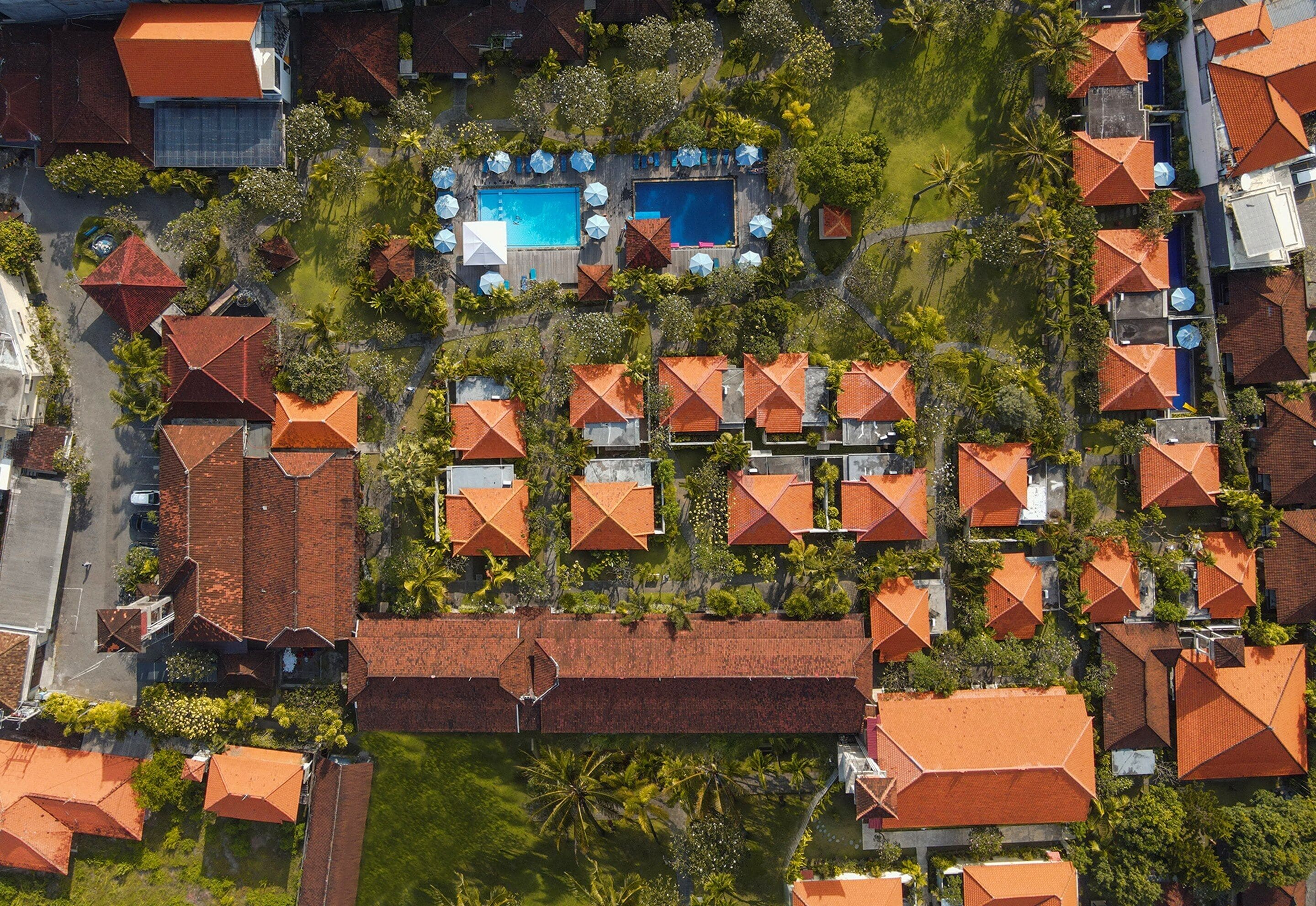 An aerial view of a resort with multiple bungalow-style buildings, a central swimming pool, and surrounding greenery.