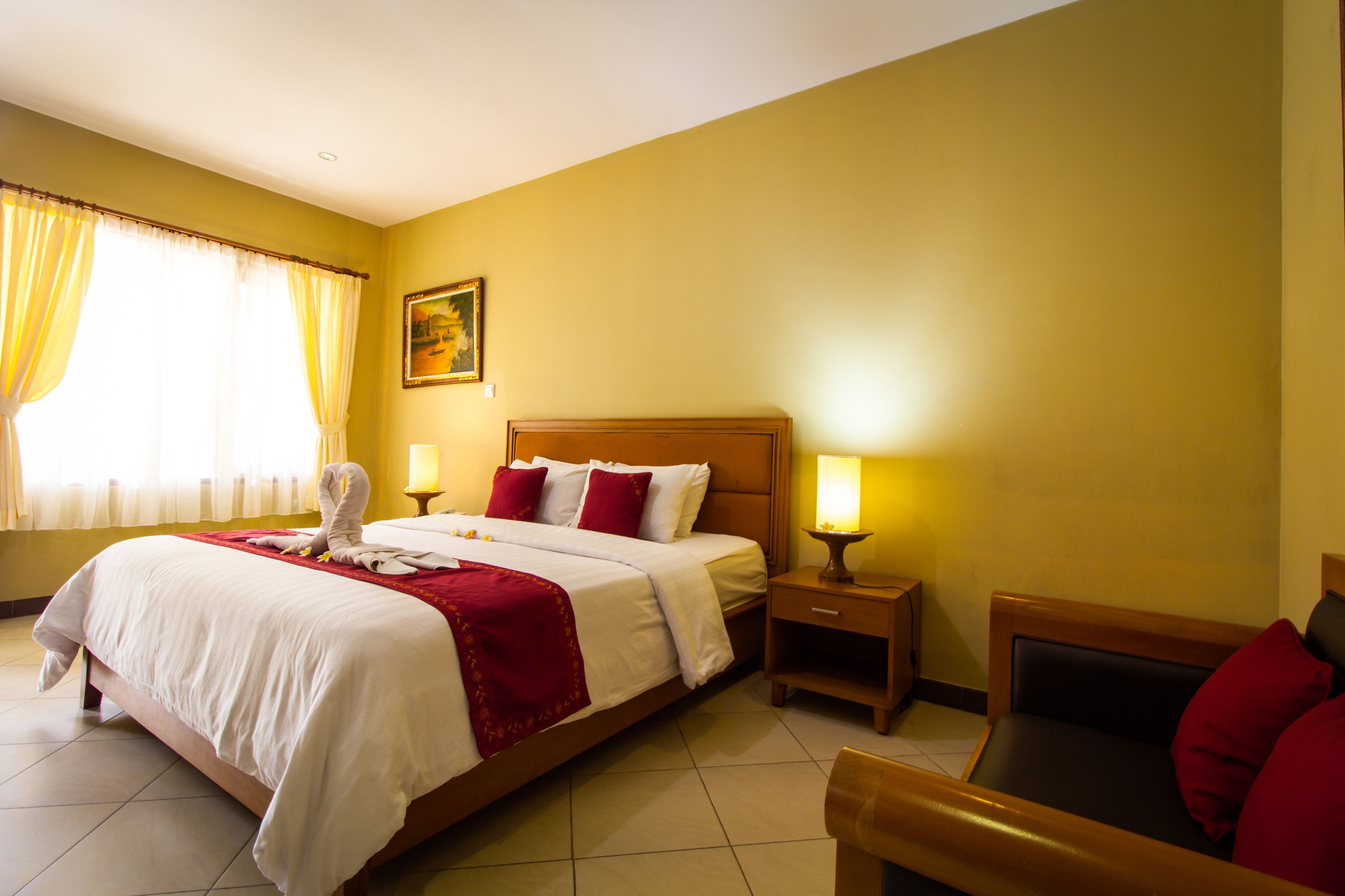 Una habitación de hotel con una cama grande, una mesita de noche con lámpara, una silla de madera y un cuadro en la pared.