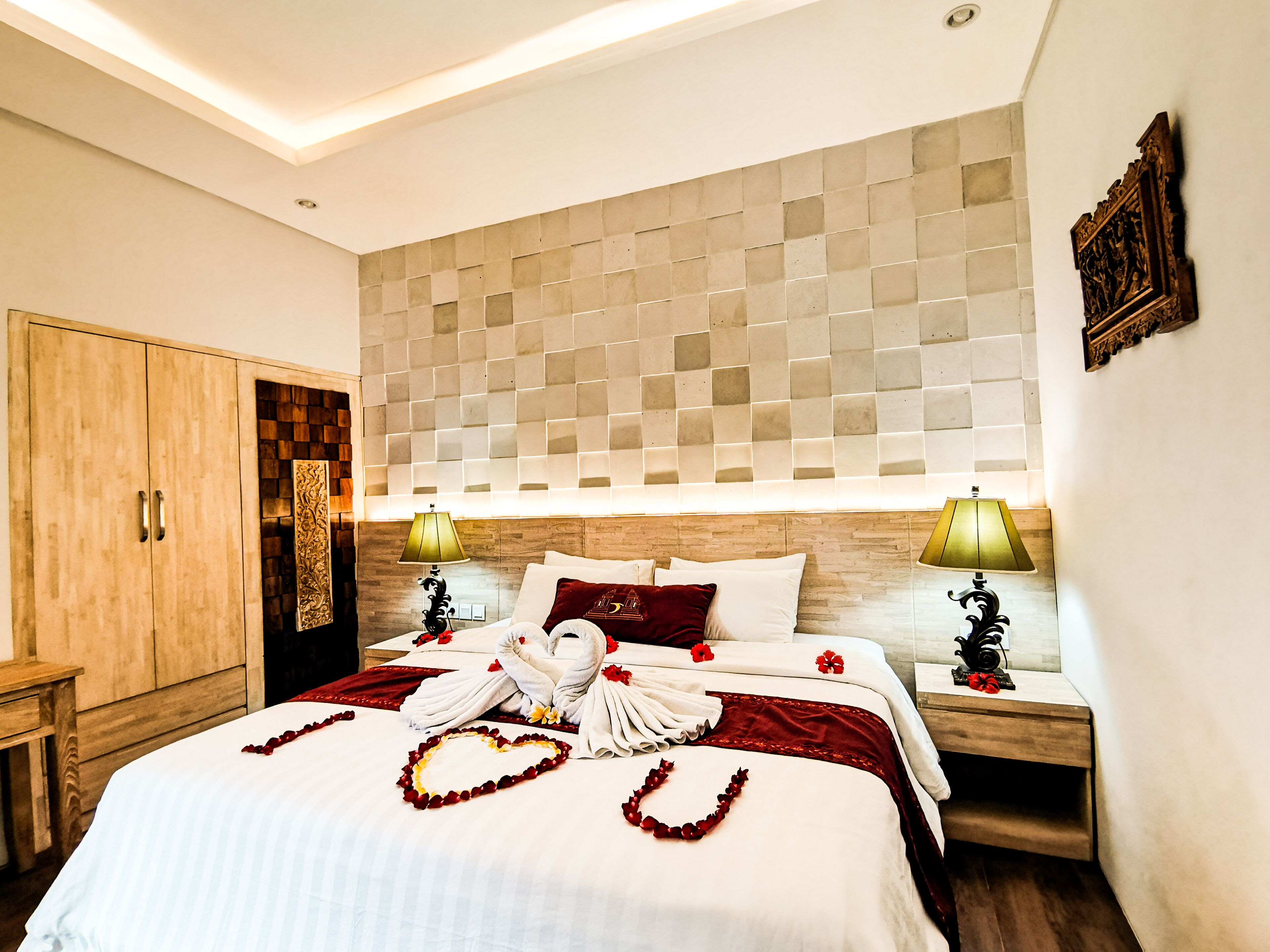 Una habitación de hotel con una cama grande, dos mesitas de noche con lámparas, un armario de madera y un cabecero decorativo.