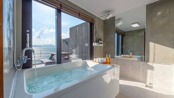 A modern bathroom with a large bathtub, a shower, and a view of the sea.