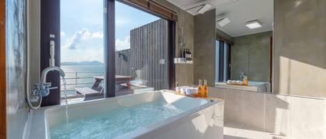 A modern bathroom with a large bathtub, a shower, and a view of the sea.