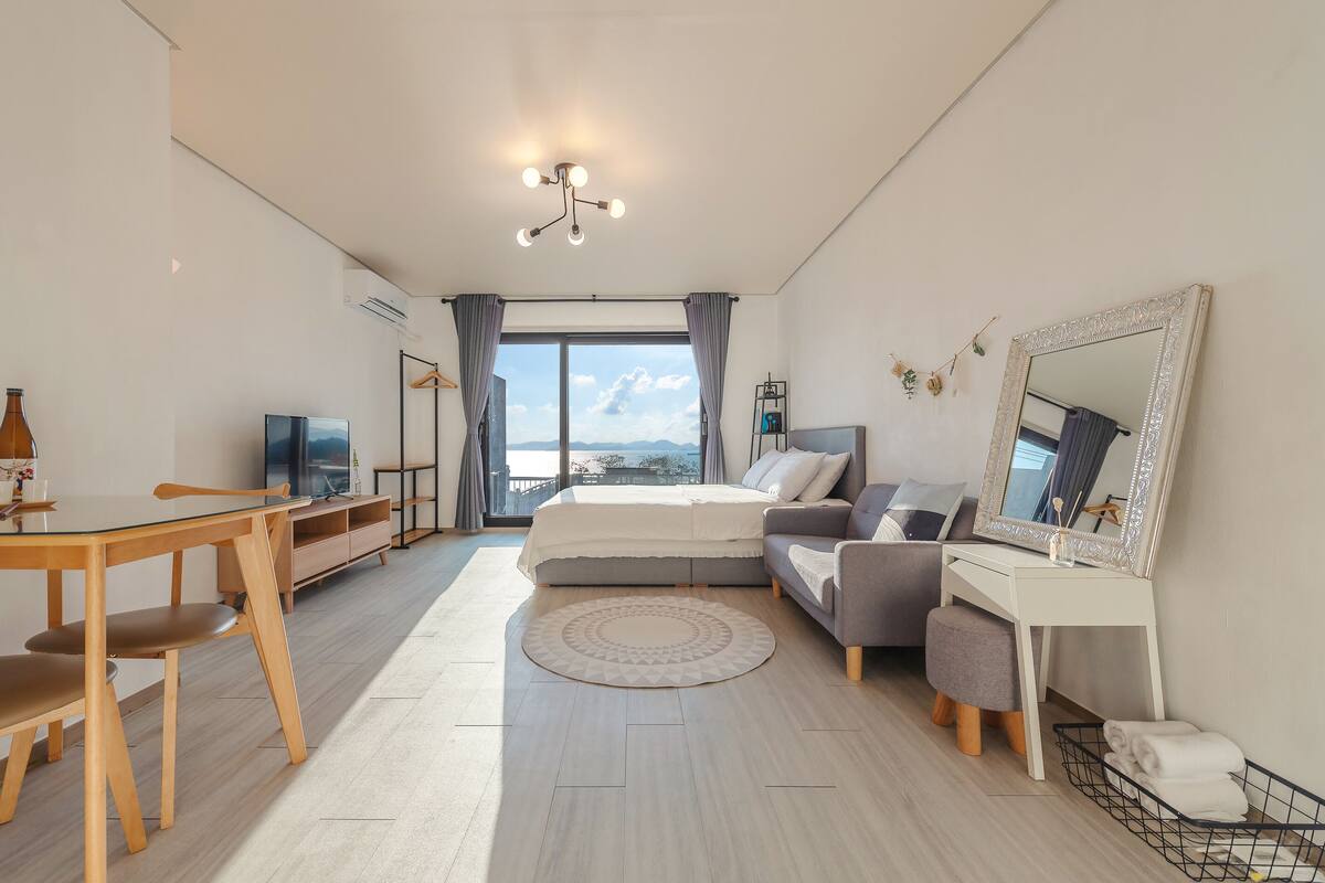 Moderni hotellihuone, jossa on sänky, työpöytä, televisio, ruokapöytä ja näkymä ulos.