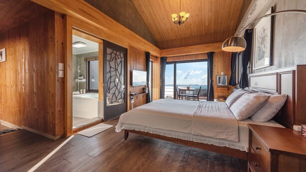 Quarto de cabana de madeira com uma cama grande, uma escrivaninha de madeira, uma cadeira e vista para o exterior.