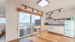 Cozinha moderna com vista para o mar, área de jantar com móveis de madeira e uma geladeira branca.
