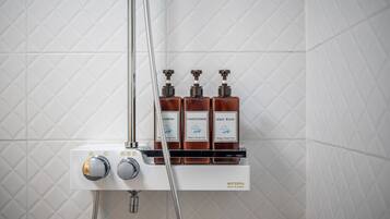 Zona de ducha con tres botellas de champú, acondicionador y gel de baño, y un panel de control con dos perillas.