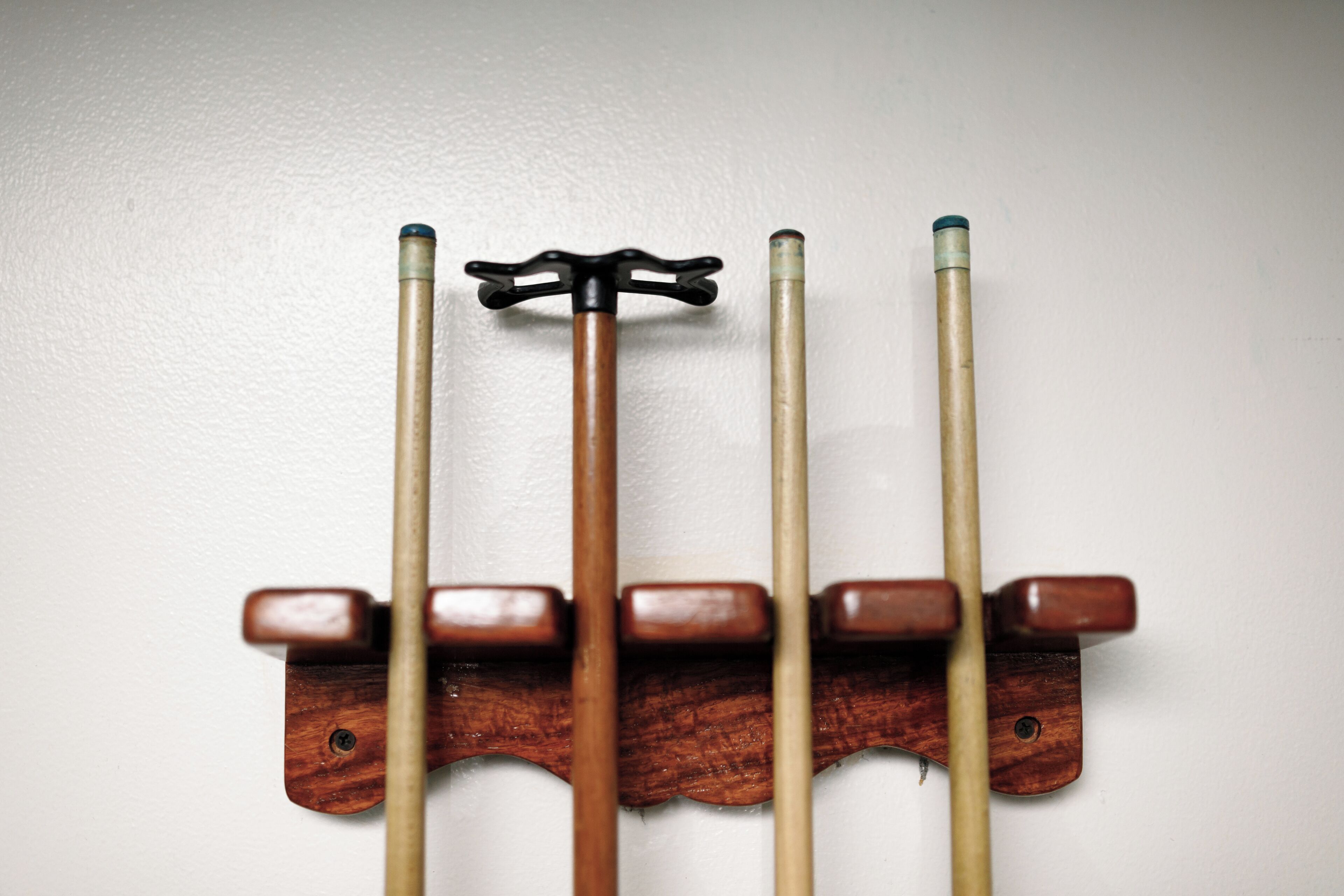 A wooden rack holding four pool cues against a white wall.