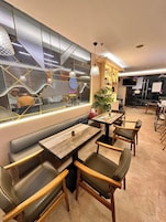 Un interior de restaurante con mesas de madera y asientos acolchados, un ventanal con un letrero de neón e iluminación colgante.