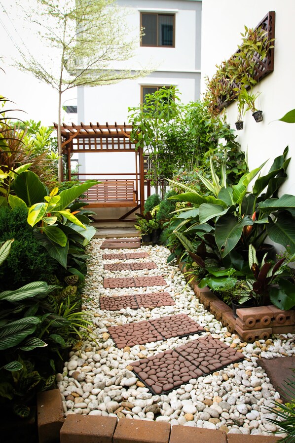 A pathway leading to a wooden gate, surrounded by various plants and a white building in the background.