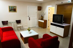 A living room with red sofas, a white coffee table, a TV on a wooden cabinet, and a door leading to another room.