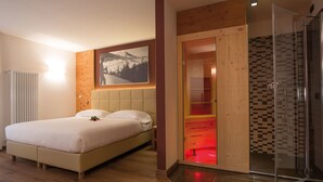 A modern bedroom with a large bed, a wooden headboard, a glass shower enclosure, and a wooden wardrobe with a red light. - Sassdei My Active Suite Hotel (Andalo)