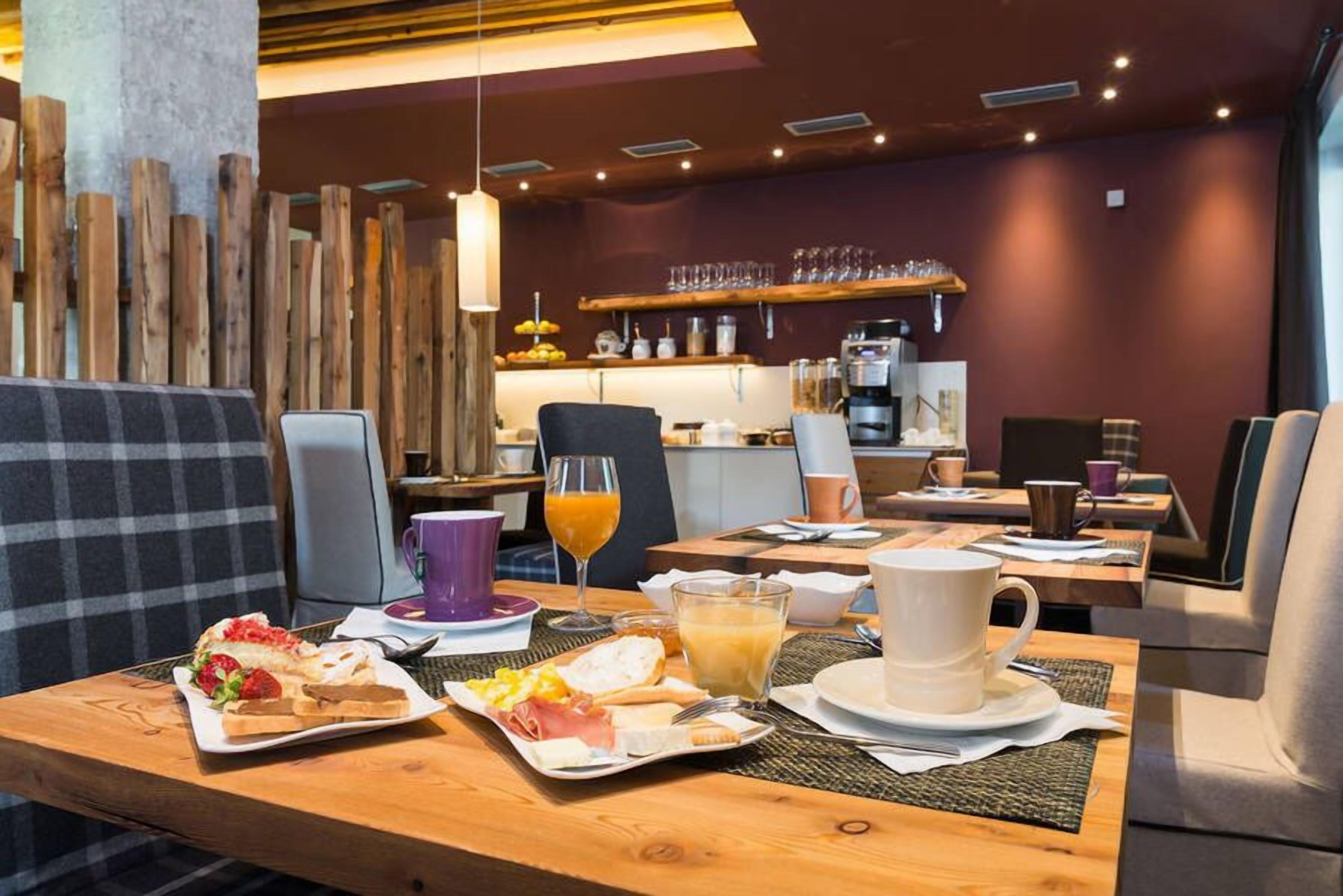 Un desayuno con una mesa de madera, sillas y una variedad de alimentos como pasteles, fruta y bebidas.