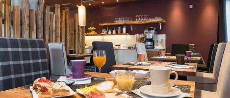 Un desayuno con una mesa de madera, sillas y una variedad de alimentos como pasteles, fruta y bebidas.