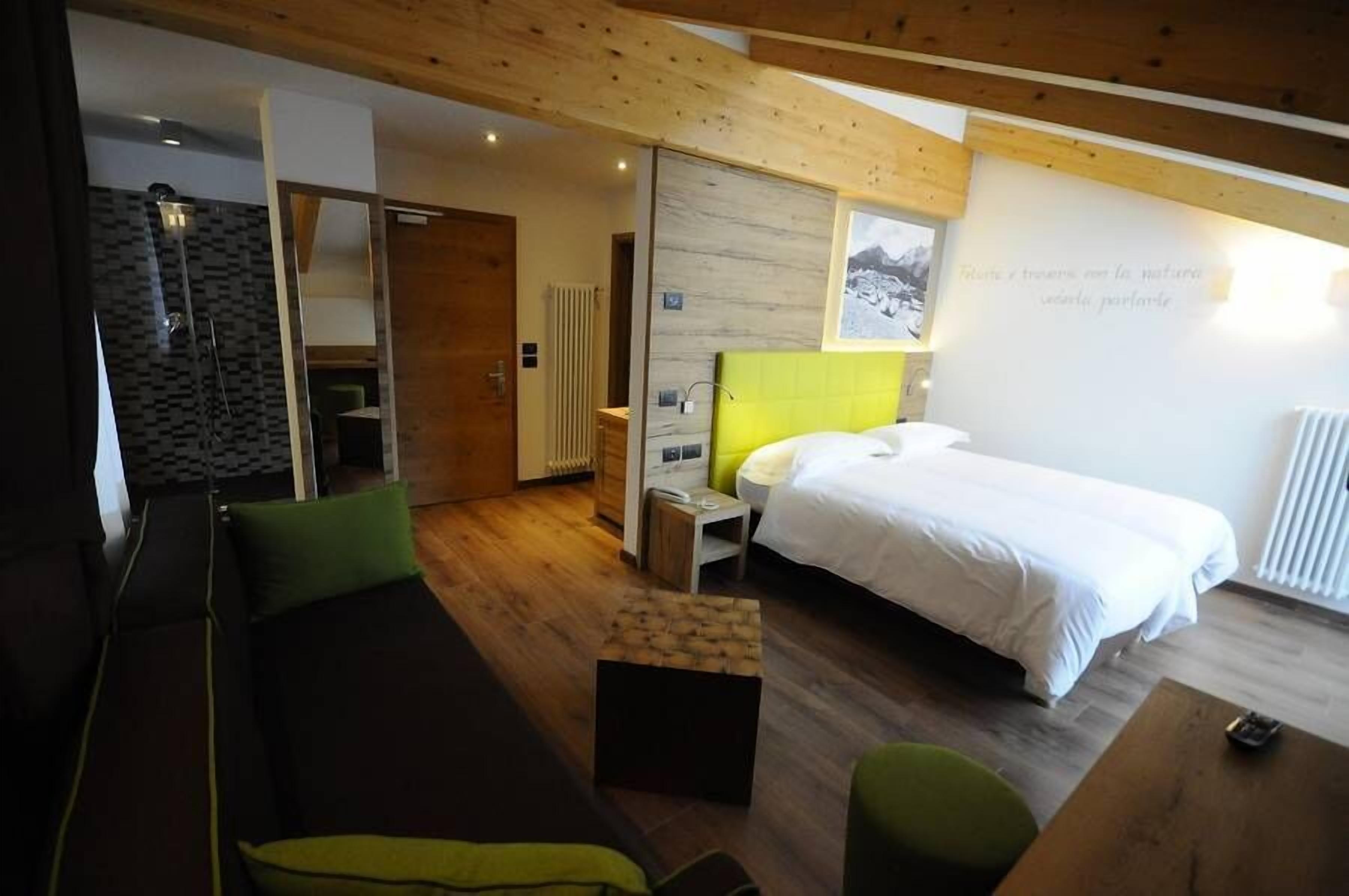 Una habitación de hotel moderna con cama, sofá, una mesita y zona de ducha.