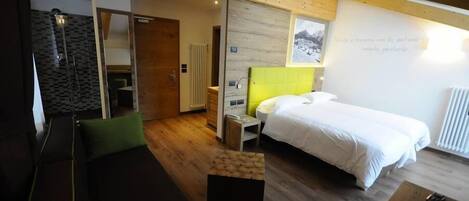 Una habitación de hotel moderna con cama, sofá, una mesita y zona de ducha.