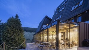 A modern building with a glass exterior, wooden deck, and outdoor seating area. - Pytloun Wellness Hotel Harrachov (Harrachov)