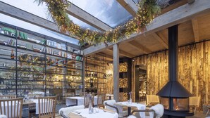 A cozy restaurant with wooden tables and chairs, a fireplace, and a bookshelf filled with books and decorative items. - Pytloun Wellness Hotel Harrachov (Harrachov)