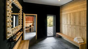 A modern bathroom with a wooden bench, a large mirror, and a sauna area.