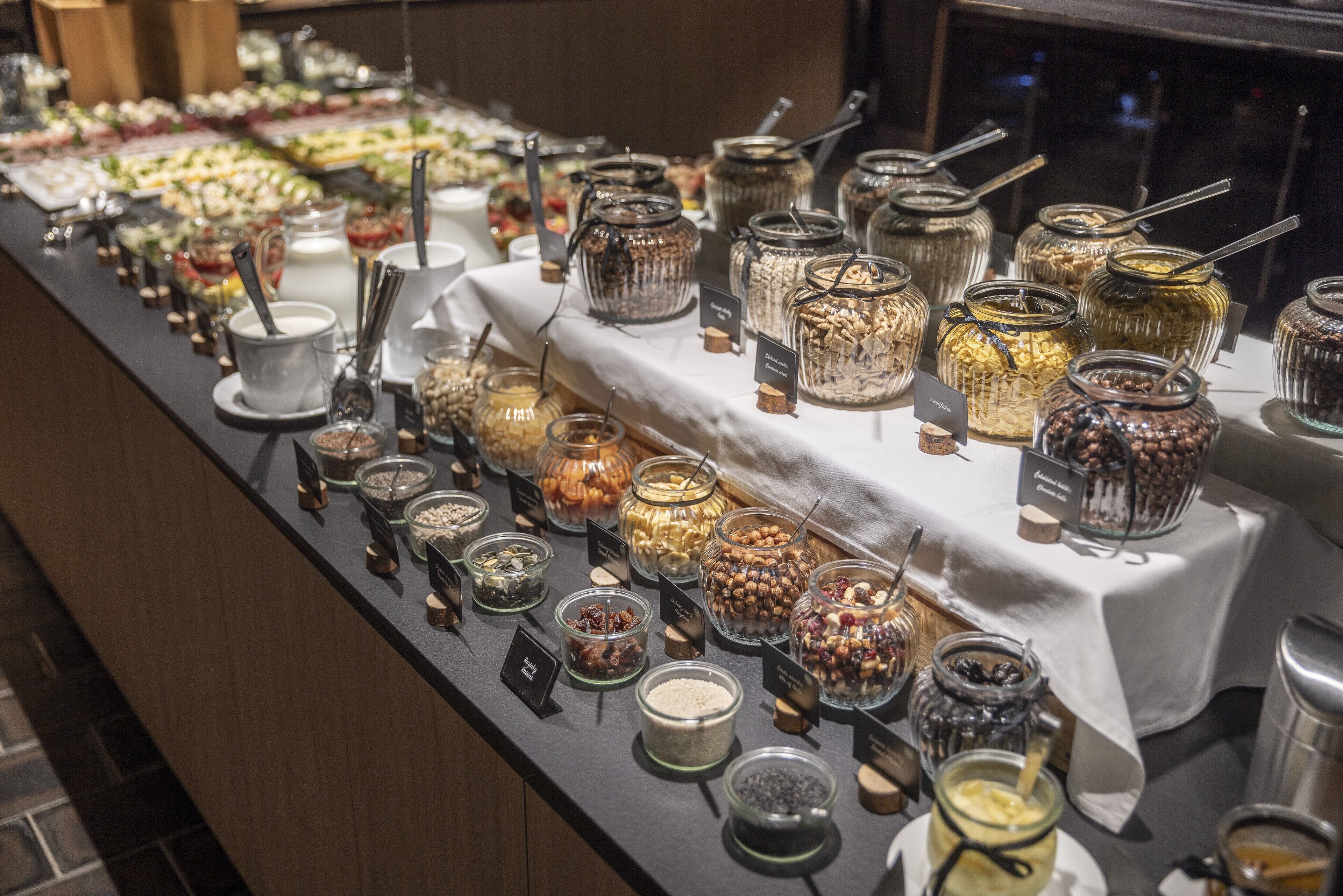 A buffet with various food items in glass containers, each labeled with a name tag.