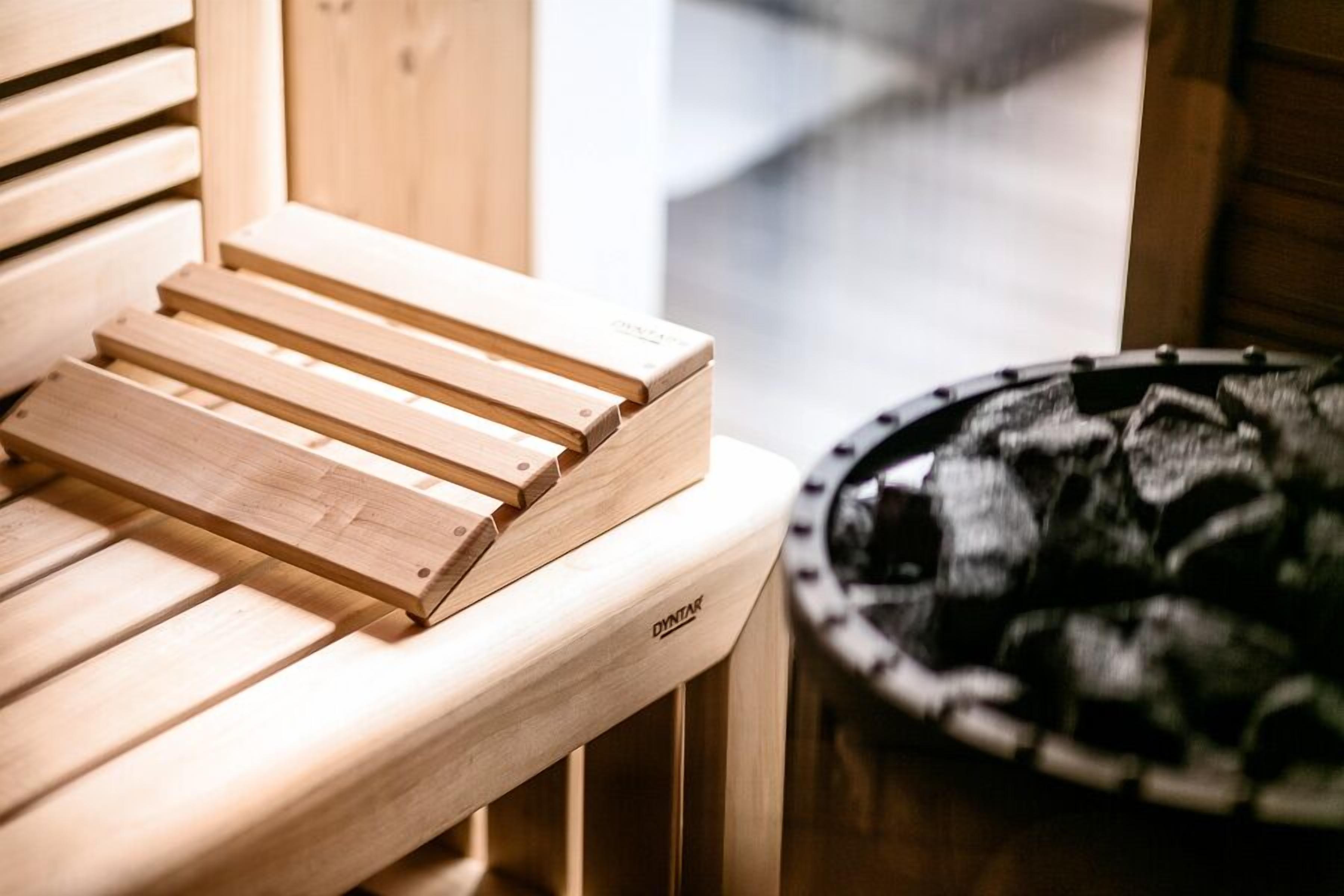 Um banco de sauna de madeira com assento e encosto, parede de sauna em madeira e chão da sauna com tapete preto.