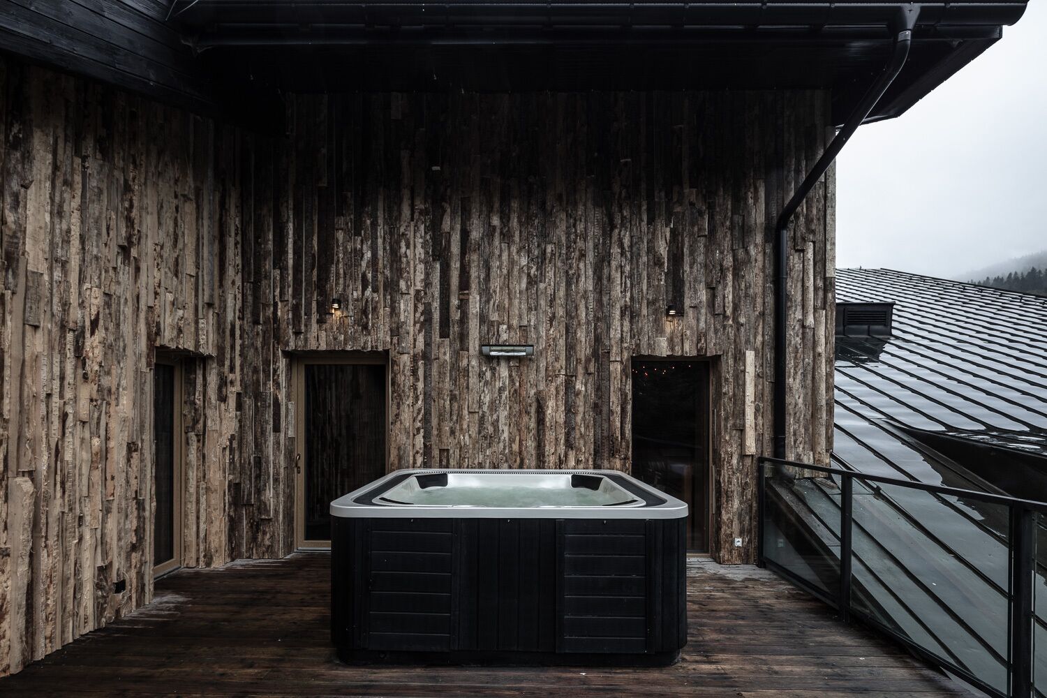 A wooden exterior with a hot tub on a deck.