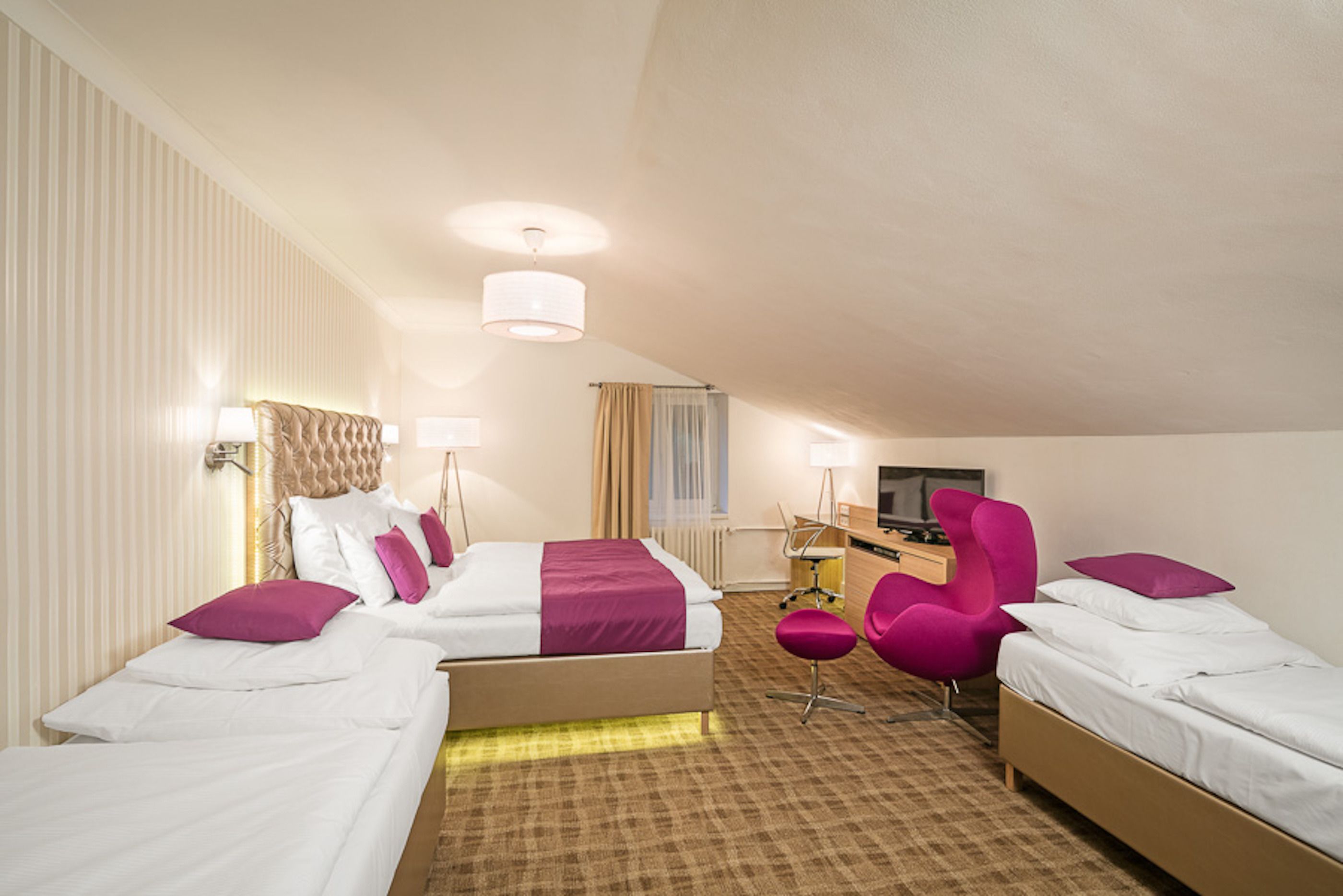 A hotel room with two beds, a desk, a chair, and a television.
