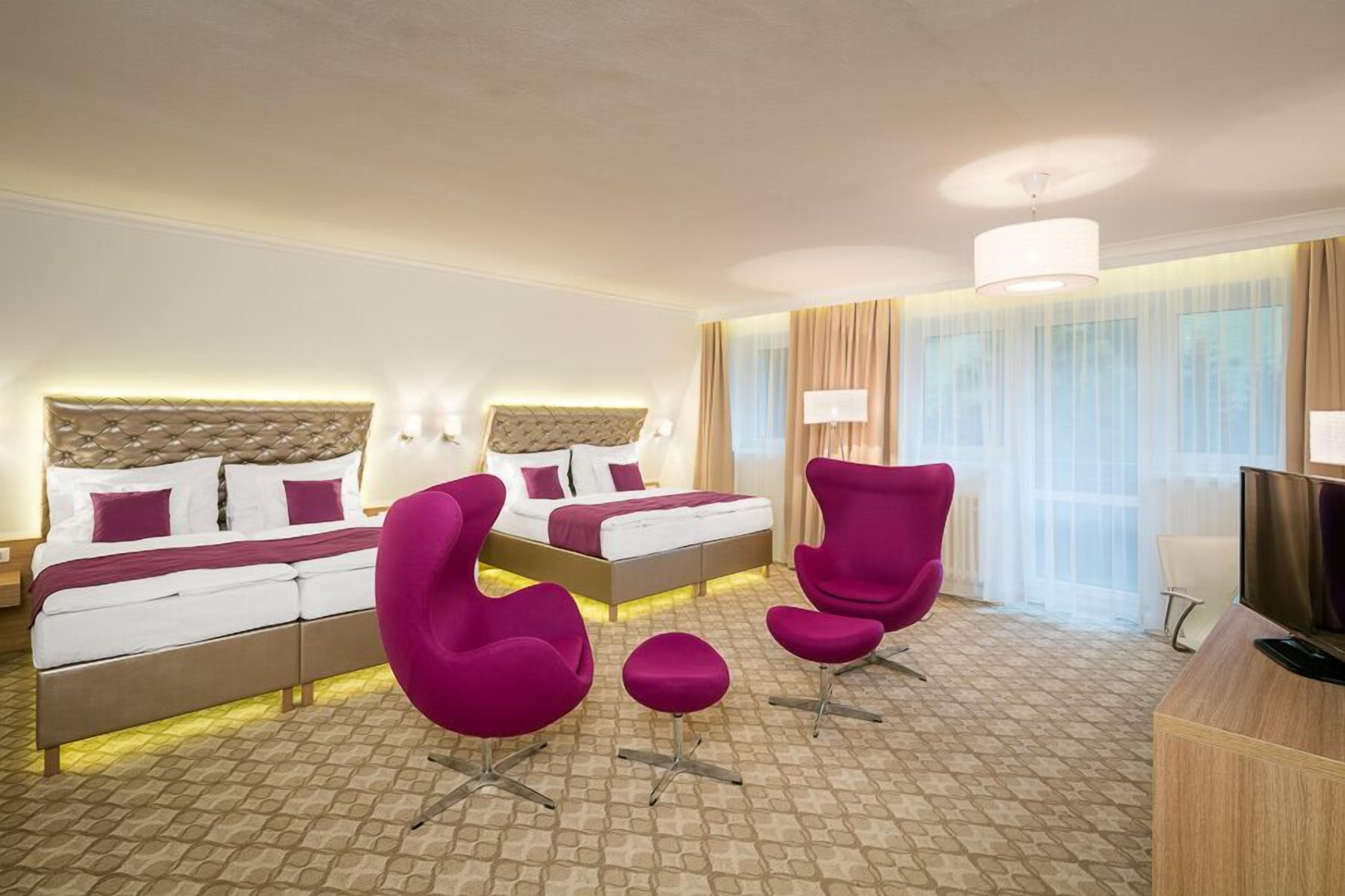 Habitación de hotel con dos camas, un escritorio, televisor y un ventanal con cortinas.