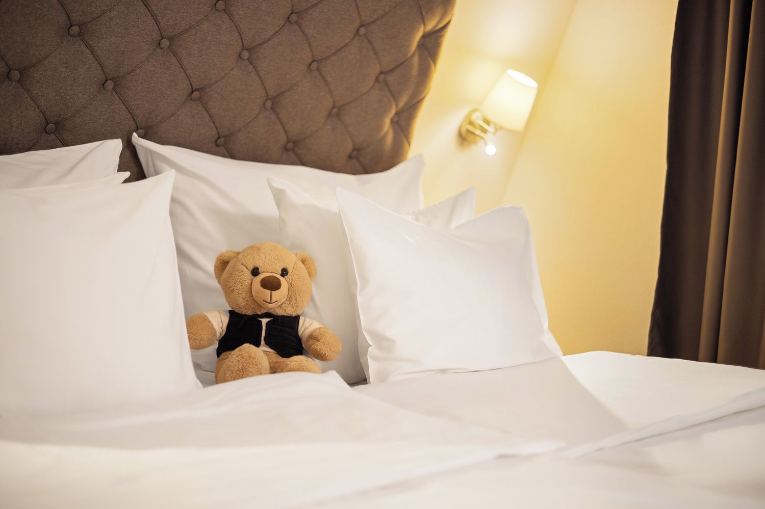 A bed with white bedding and a teddy bear in the center.