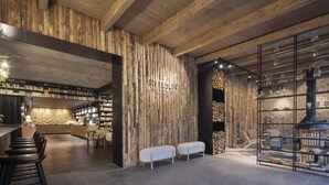 A modern interior with exposed wooden beams, a bar area with stools, a seating area with white benches, and a display of glassware. - Pytloun Wellness Hotel Harrachov (Harrachov)