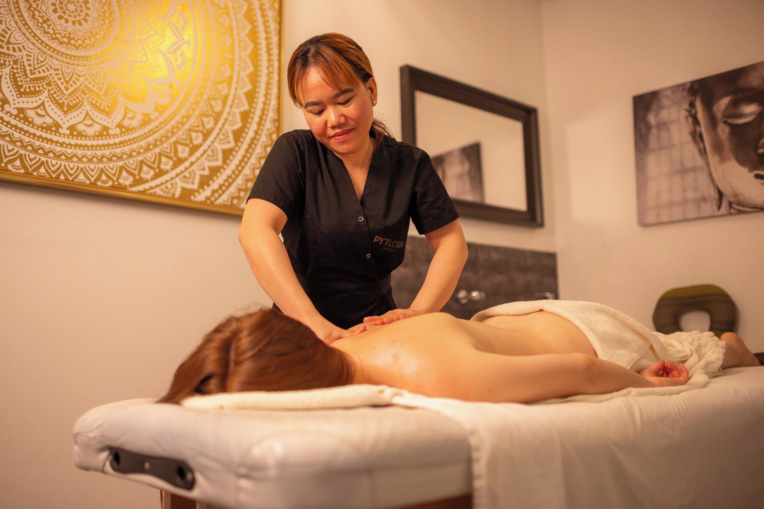 A massage therapy session in a room with a patterned tapestry, framed artwork, and a massage table.