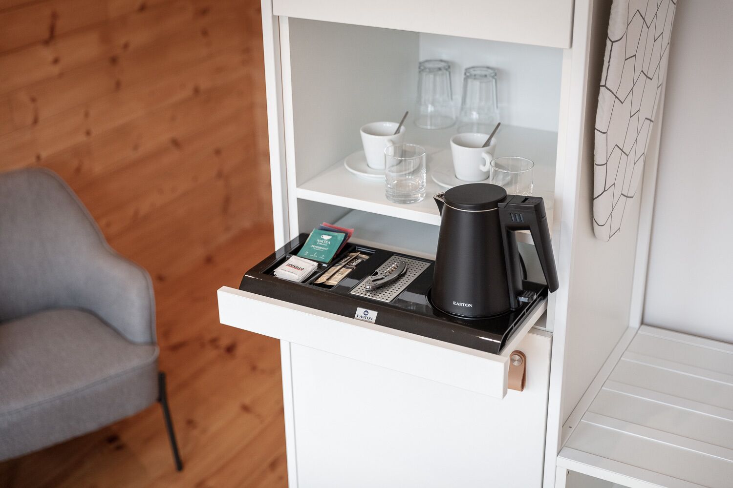 A hotel room with a minibar, a coffee maker, and a chair.