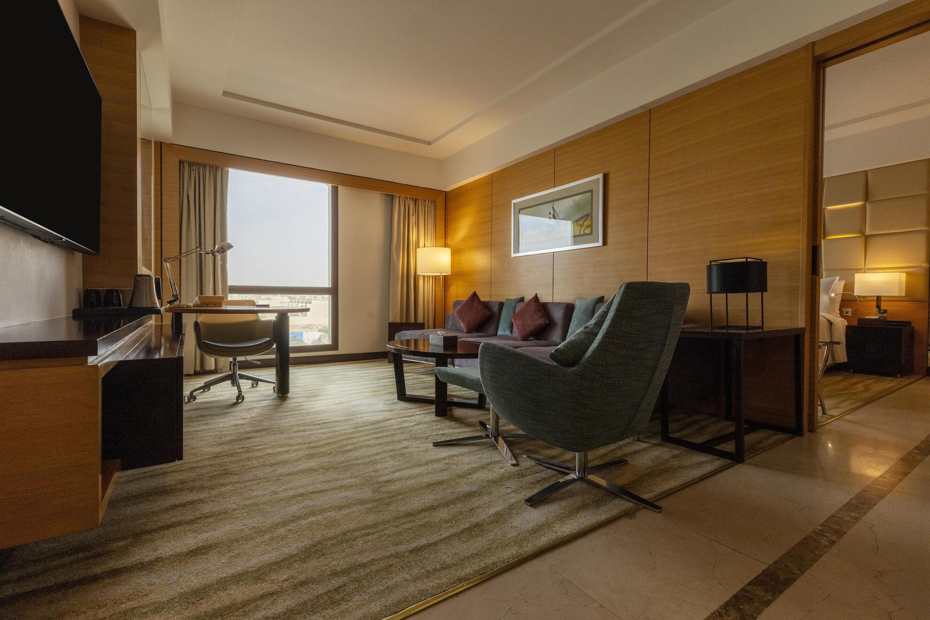 Una habitación de hotel moderna con sofá, sillón, escritorio y un ventanal con vistas a la ciudad.
