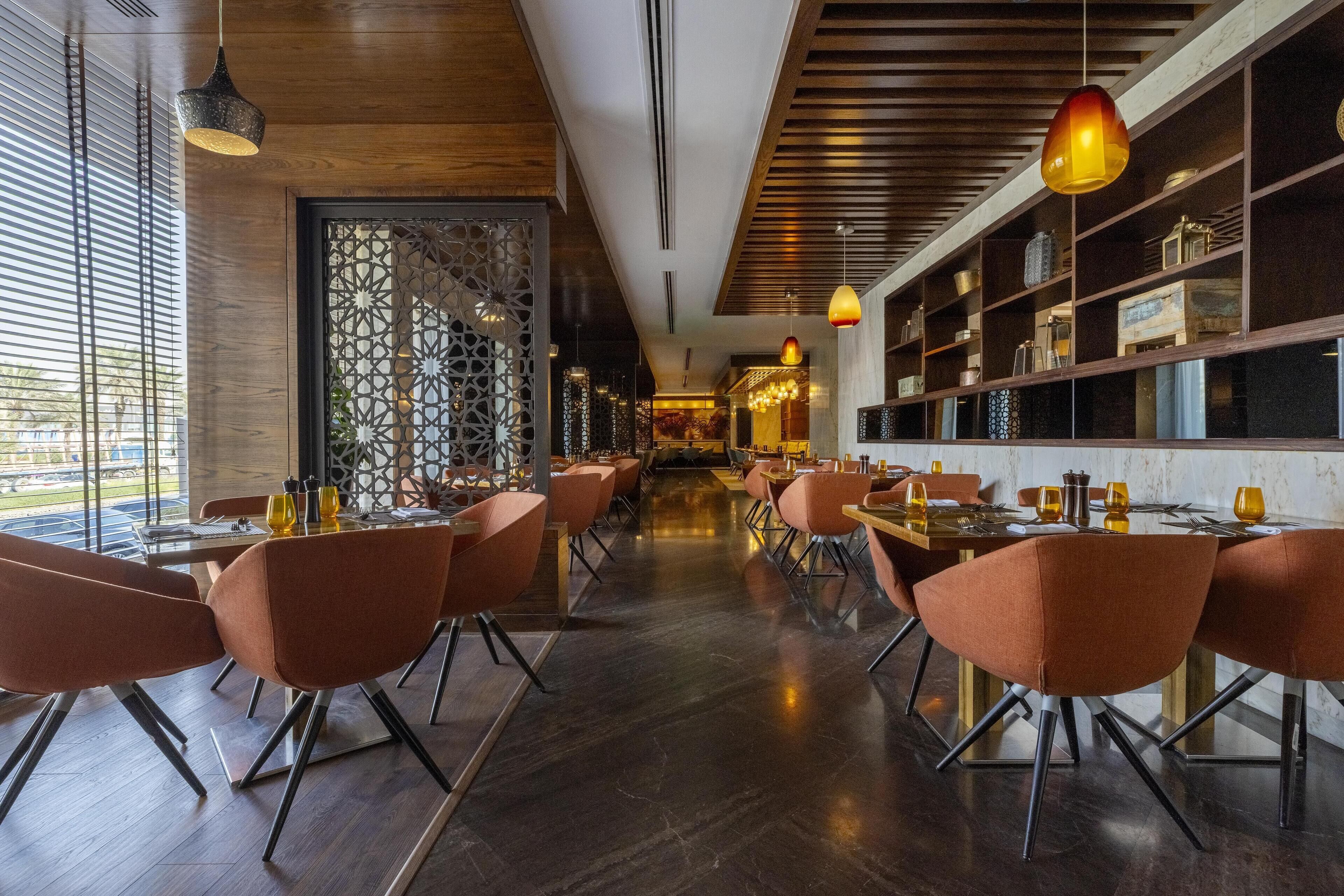 A modern restaurant interior with wooden flooring, orange chairs, and pendant lighting.