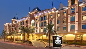 Um hotel com uma placa visível, várias varandas e uma entrada bem iluminada.