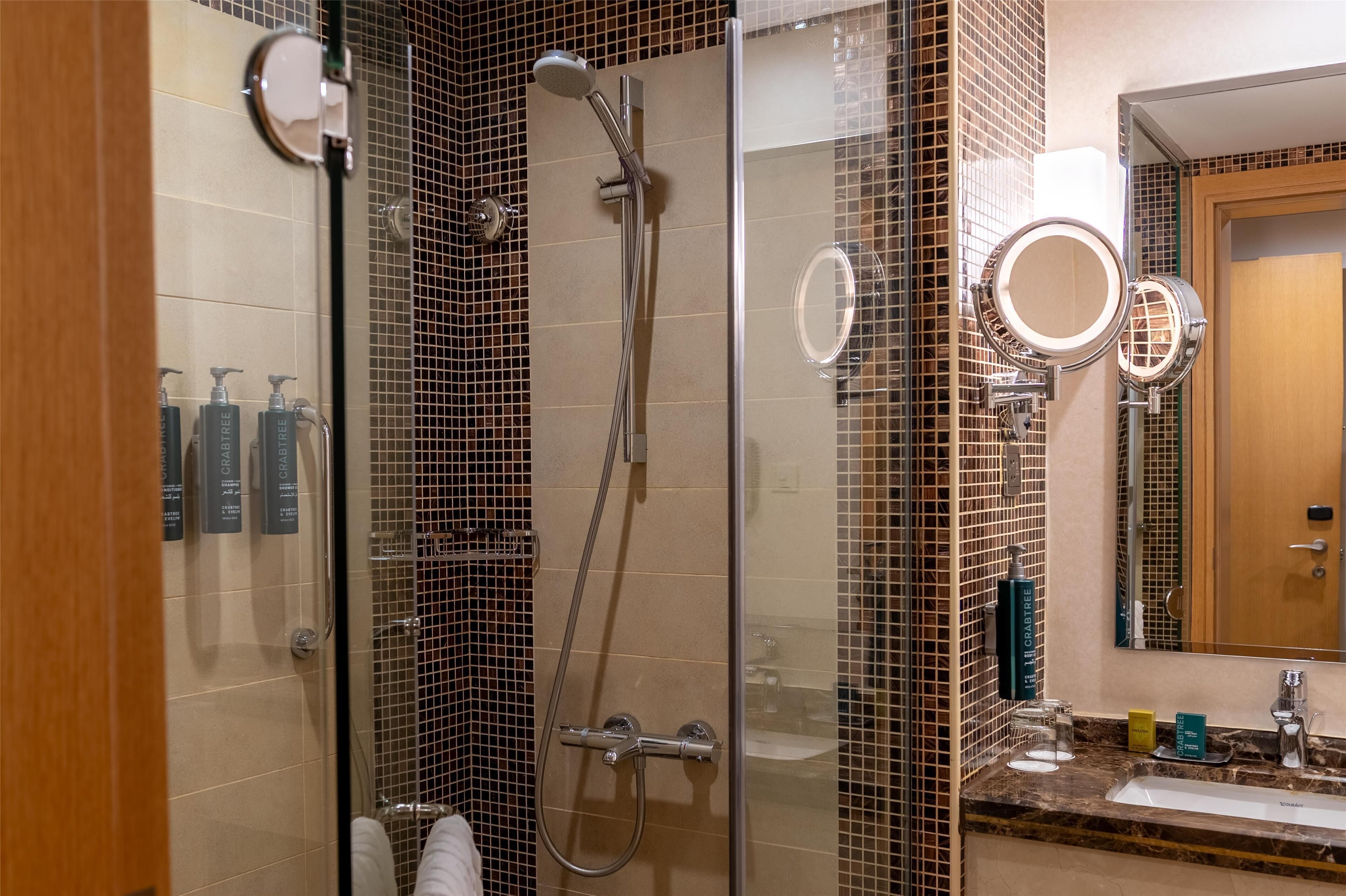 Un bagno moderno con cabina doccia in vetro, lavabo con piano in marmo e specchio a cornice rotonda.