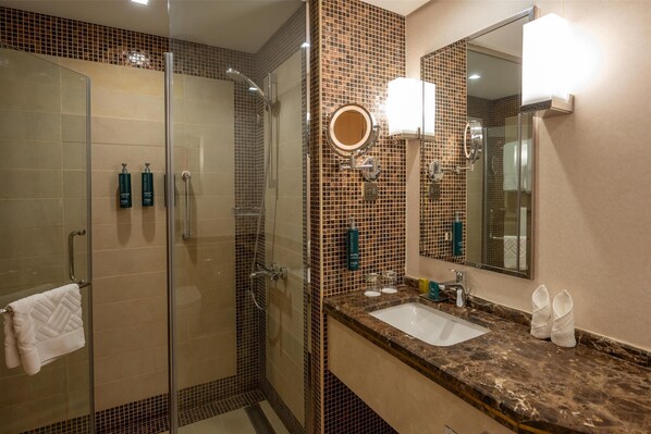 Une salle de bain moderne dotée d’une douche à parois de verre, d’un lavabo avec un plan de travail en marbre et d’un grand miroir à cadre rond.