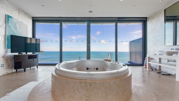 Une salle de bain moderne dotée d’une grande baignoire, d’un téléviseur et offrant une vue sur l’océan.