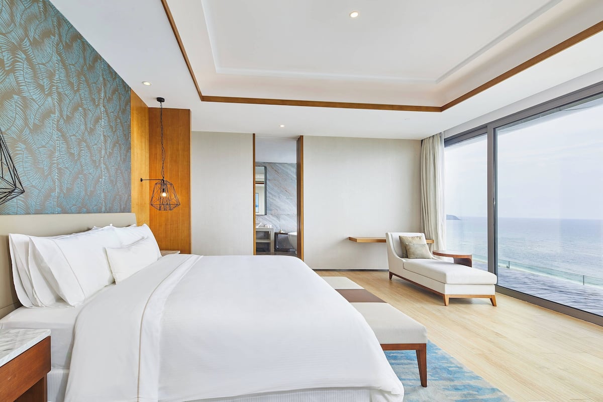 Une chambre d’hôtel moderne dotée d’un grand lit, d’un coin salon avec vue sur la mer et d’un mur décoratif en bois.
