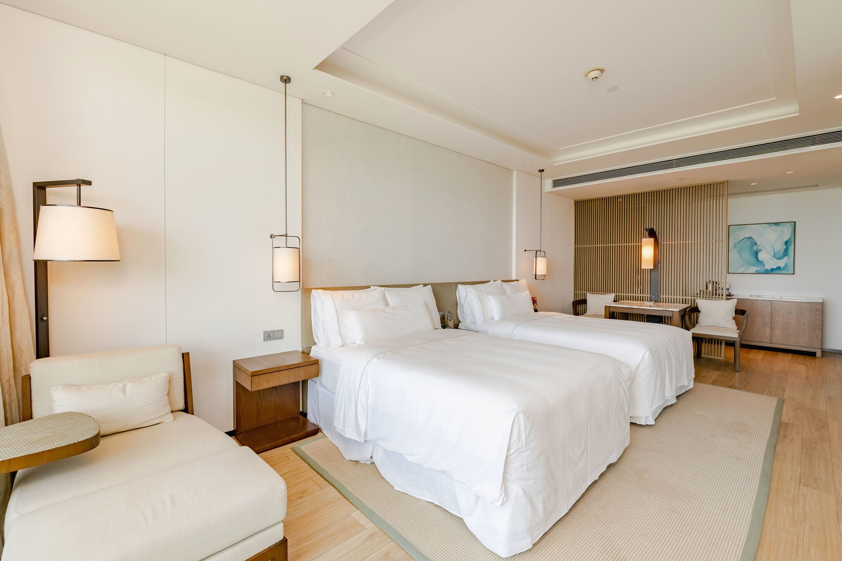 Une chambre d’hôtel moderne avec deux lits, un coin salon et un bureau.