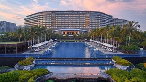 Un grand hôtel doté d’un espace piscine, de palmiers et d’une façade incurvée.