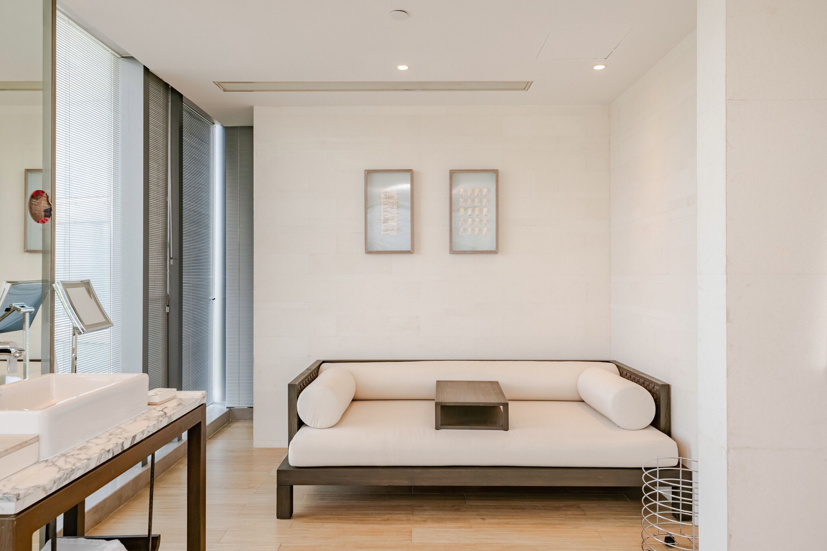 A modern bathroom with a large mirror, a sink, a wooden bench, and two framed artworks on the wall.