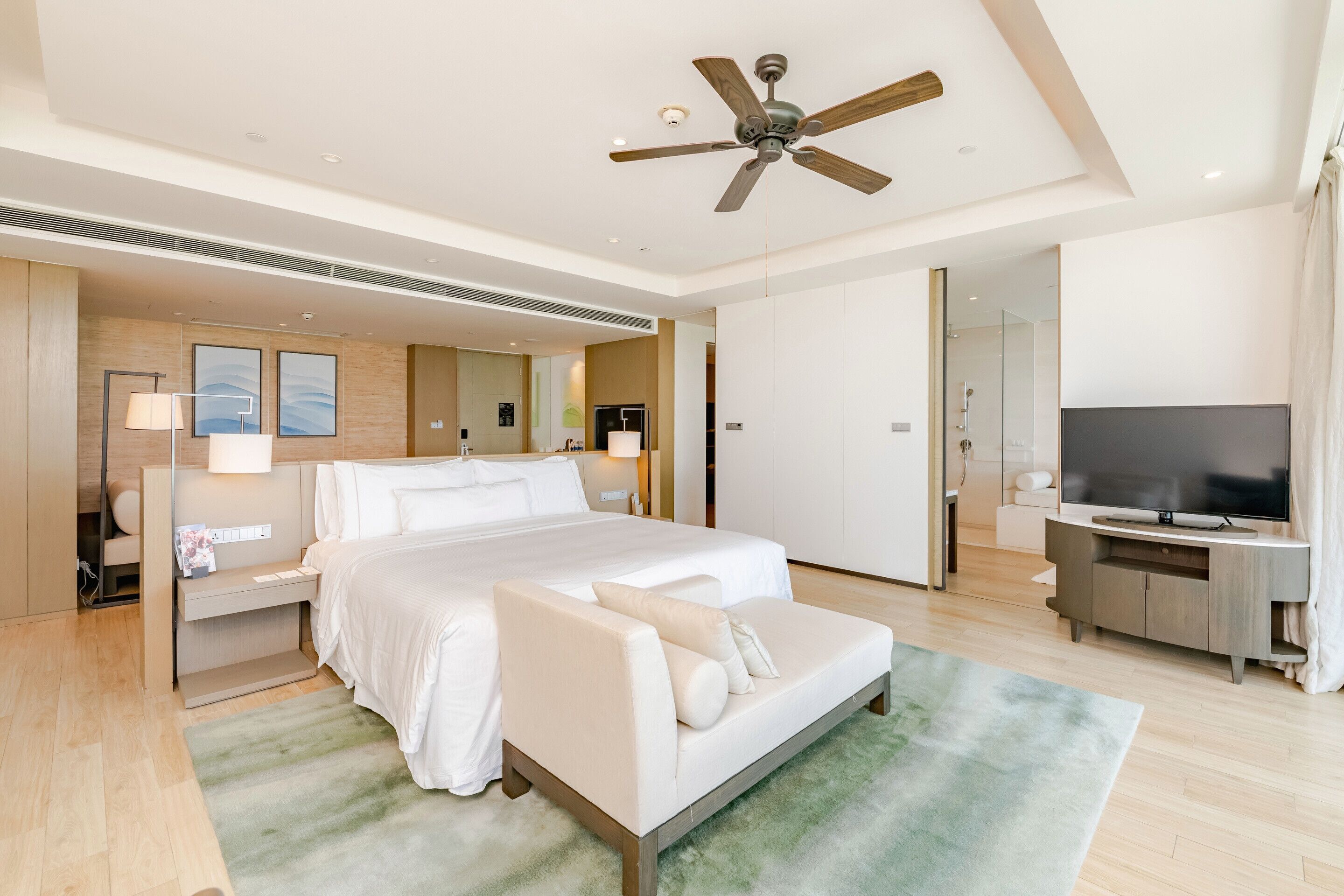 A modern hotel room with a large bed, a sofa, a TV, and a ceiling fan.