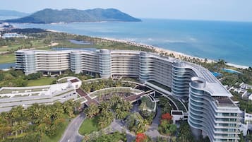 A modern hotel with multiple curved balconies, a landscaped garden, and a view of the ocean.