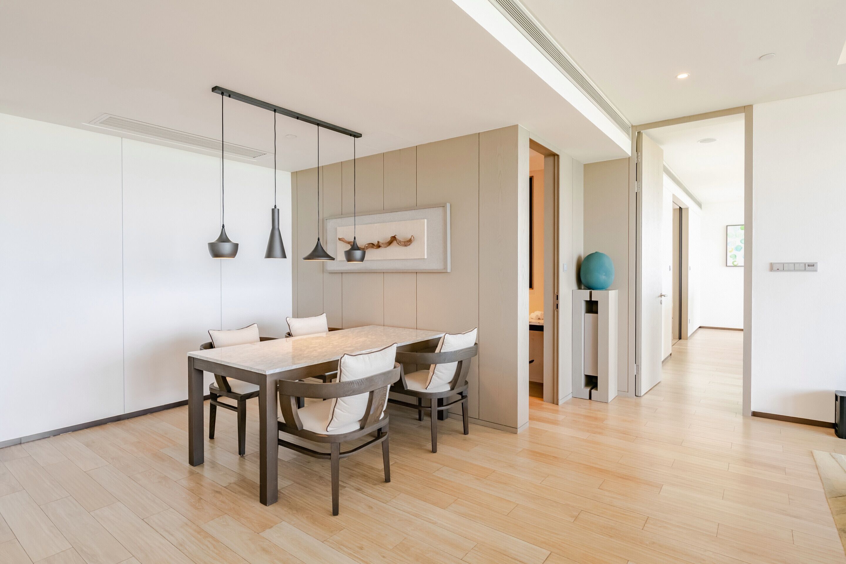 A modern dining area with a wooden table and chairs, pendant lights, and a framed artwork on the wall.