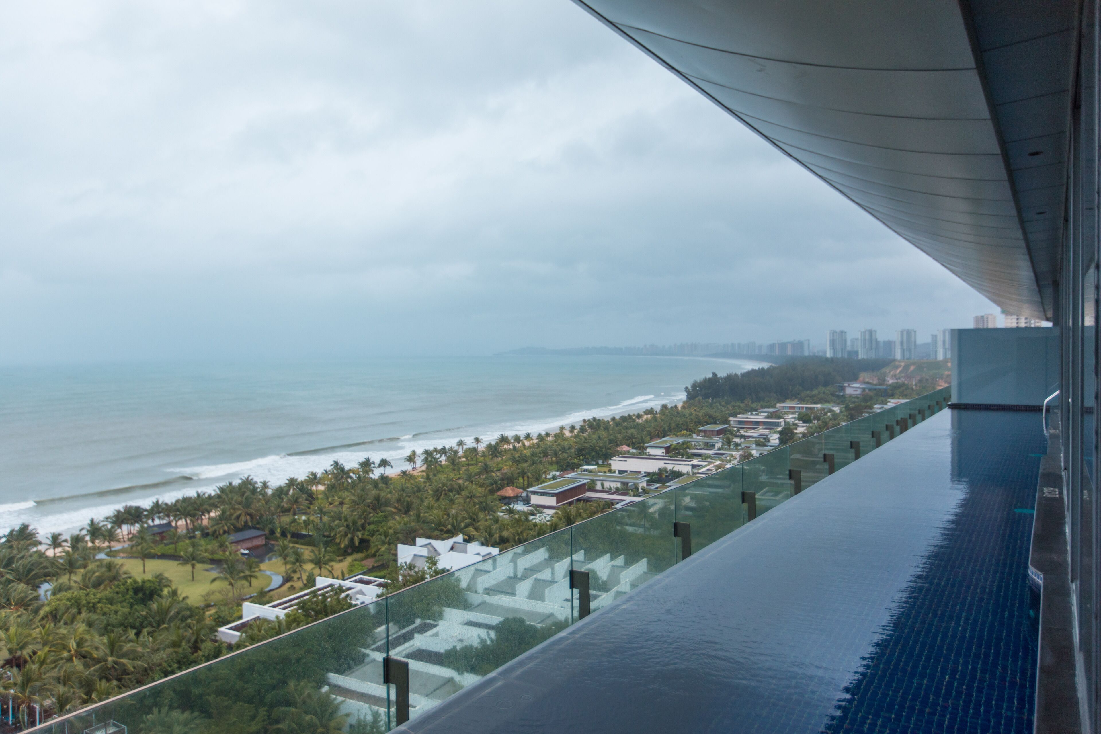 Um edifício alto com varanda de vidro, vista para a praia e horizonte urbano.