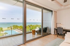 Une chambre d’hôtel moderne dotée d’une grande porte-fenêtre coulissante donnant sur un balcon avec vue sur l’océan et une piscine.