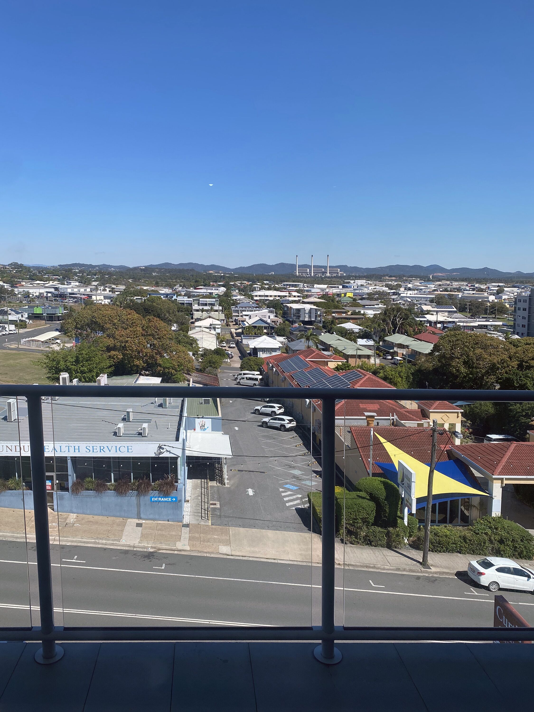A view of a cityscape with a clear sky, a hospital building, and a road with parked cars.