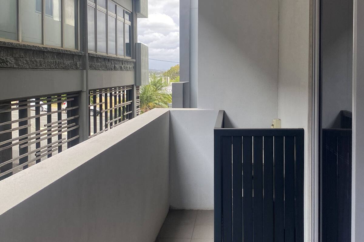 A balcony with a view of a building, a metal railing, and a tiled floor.